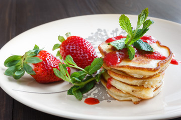 Freshly pancakes with garden fresh strawberries and mint on a bright plate, photographed in daylight natural light.