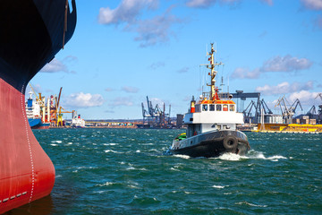 A cargo ship with the assistance of a tugboat in port.