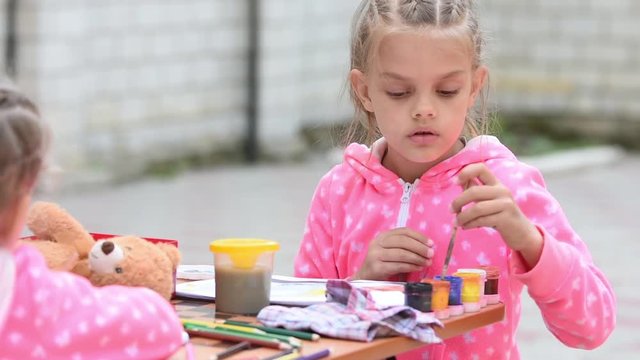 Seven-year girl choose the right color ink drawing in an album, sitting at a table with another girl