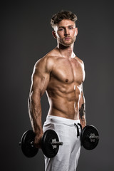 Fototapeta na wymiar Handsome young bodybuilder training withdumbbells, on grey
