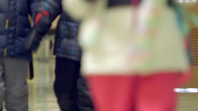 Young elementary school kids walking through the hall of their school with winter coats and boots.