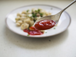 Spoon with ketchup in front of plate with meat dumplings out of focus.