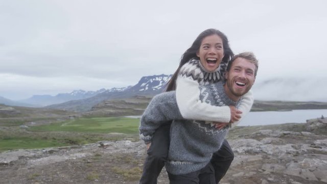 Happy couple having fun on Iceland laughing joyful and playful wearing Icelandic sweaters doing piggyback. Woman and man model enjoying nature landscape on Iceland. RED EPIC SLOW MOTION.