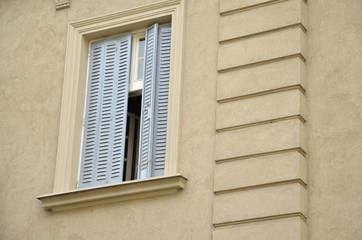 Semi closed white jalousie on a window on a yellow building facade