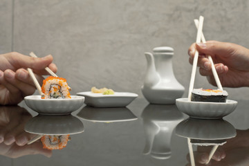 hands holding sushi with chopsticks at restaurant