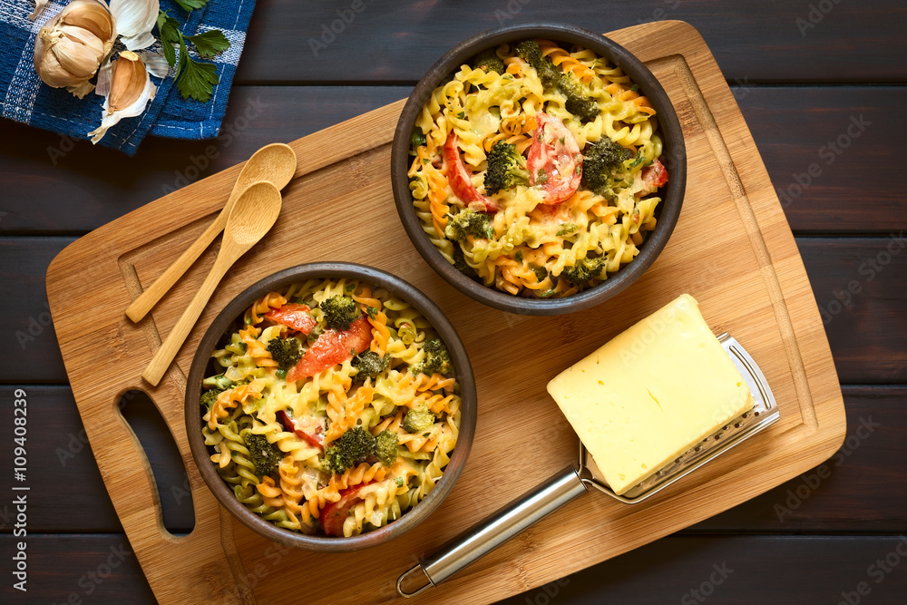 Canvas Prints Baked tricolor fusilli pasta and vegetable (broccoli, tomato) casserole in rustic bowls, with grater, cheese and spoons on wooden board, photographed overhead on dark wood with natural light