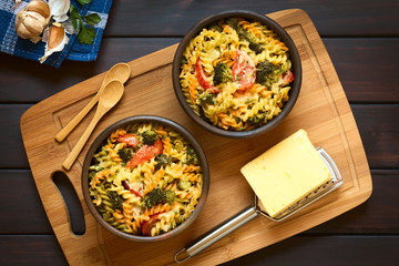 Baked tricolor fusilli pasta and vegetable (broccoli, tomato) casserole in rustic bowls, with...