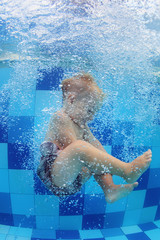 Funny photo of baby boy swimming and diving in pool with fun - jumping deep down underwater with splashes and foam. Children water sports activity and swimming lessons with parents.
