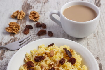 Cooked millet groats on white plate and cup of coffee with milk, healthy food and nutrition