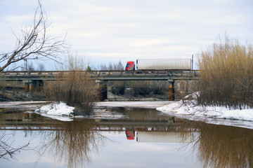 Fototapeta premium Truck driving on a bridge over river in the spring.