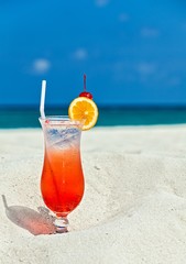 Glass of cocktail is on sandy coral  beach