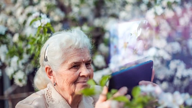 Elderly woman shoots video on tablet with hologram. Technology concept.