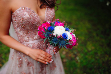 Colorful bouquet of peonies is holding the bride in pink dress