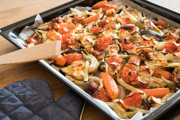 Roasted vegetables and cheese in a baking tray and a wooden spoon with an oven glove