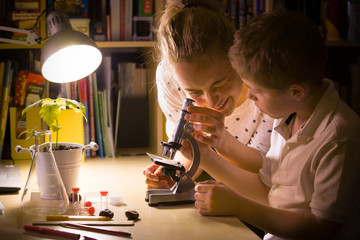 Young mother and elementary school kid boy looking into microscope at home. Family studying samples...