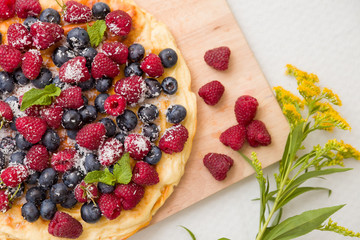 Fresh berries on the tart cake from above. Delicious homemade pie with organic raspberries and blueberries and summer flowers on wooden board. Summer dessert and snack.