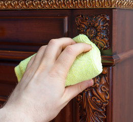 Man's hand wipes dust from antique furniture.