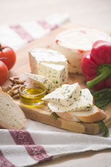 Variety of home made cheese and paprica and herbs, olive oil, olives and bread on a wooden board. brined curd white cheese with vegetables on the table