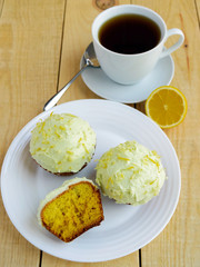 Light lemon cupcakes muffins on wooden background and a cup of tea.