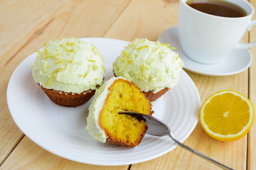 Light lemon cupcakes muffins on wooden background and a cup of tea.