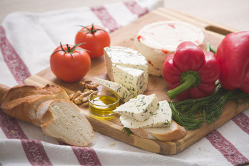 Variety of home made cheese and paprica and herbs, olive oil, olives and bread on a wooden board. brined curd white cheese with vegetables on the table
