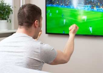 Goal! Man watching football match on television at home.