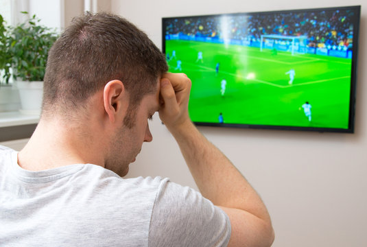 Sad man watching football match on television at home.