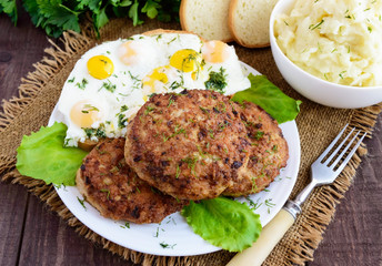 Juicy home cutlets (beef, pork, chicken) fried eggs and mashed potatoes on a wooden background.