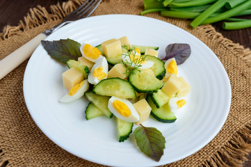 Light Italian Spring salad with fresh cucumber, quail eggs, mozzarella, olive oil on a white plate on a wooden background. Dietary meal