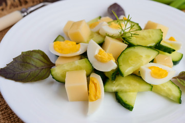 Light Italian Spring salad with fresh cucumber, quail eggs, mozzarella, olive oil on a white plate on a wooden background. Dietary meal.