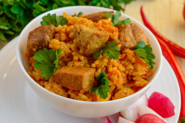 Traditional Asian sharp pilaf with fresh herbs, garlic, carrots and meat in a white bowl on a wooden background