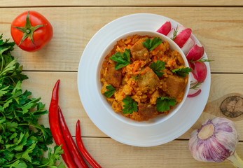 Traditional Asian sharp pilaf with fresh herbs, garlic, carrots and meat in a white bowl on a wooden background