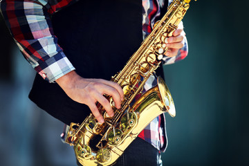 Young man playing on saxophone outside near the old wall