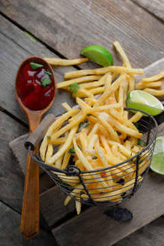French fried potatoes in metal basket with sauce and lime on cutting board