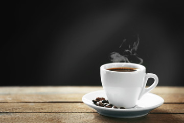 Tasse Kaffee und Kaffeekörner auf Holztisch, auf grauem Hintergrund