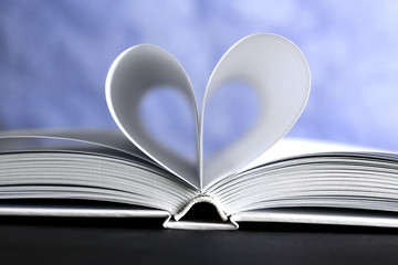 Sheets of book curved into heart shape on unfocused blue background