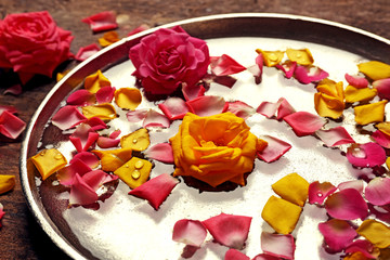 Obraz na płótnie Canvas Pink and yellow rose petals in silver bowl with water on wooden background
