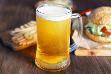 Glass mug of light beer with snacks on dark wooden table, close up
