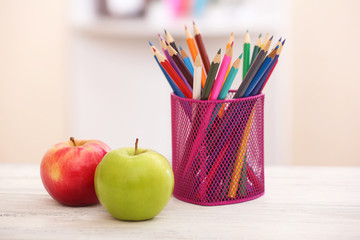 Two apples and organizer with pencils on table in the room
