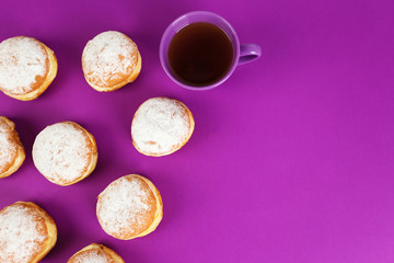 Delicious donuts with powdered sugar and cup of tea on purple surface, top view