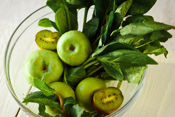 Fototapeta na wymiar The concept of a healthy and healthy meal: fresh green apples, spinach, mint and kiwifruit in a glass bowl on wooden background