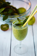 Healthy green smoothie from apples, spinach and kiwi with mint in a glass with a straw on wooden white table
