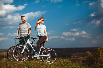Obraz premium Beautiful young couple in love walking with bicycles, looking towards the beautiful nature and the blue sky. The concept of active rest