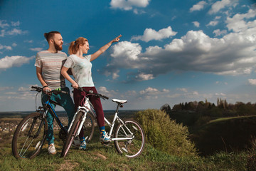 Beautiful young couple in love walking with bicycles, looking towards the beautiful nature and the blue sky. The concept of active rest