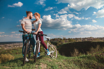 Obraz premium Beautiful young couple in love walking with bicycles hugging and looking at each other. The concept of joy and happiness