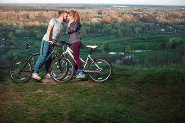 Obraz premium Beautiful young couple in love walking with bicycles, kissing and hugging. Stand near the bikes. The concept of active rest