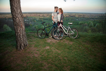Obraz premium Beautiful young loving couple hugging at sunset, there are two bikes. The concept of happiness, peace and love