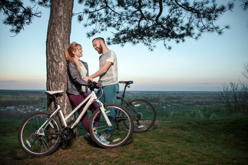 Obraz premium A young couple in love standing under a tree and hugging at sunset, standing next to the bike