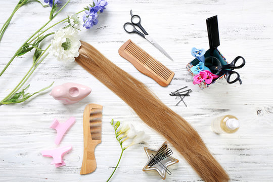 Strand of hair with flowers and barber tools on light wooden background