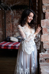 Bride's morning in a loft. Beautiful brunette young woman in a white negligee in a morning
